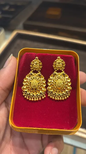 A phone photo of the earrings face-up in a velvet box, held over a shop counter.